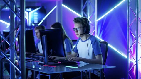 Team of Professional eSport Gamers Playing Video Games on a Cyber Games Tournament. Girls and Boys Have Headphones On, Arena is Lit with Neon Lights. Shot on RED EPIC-W 8K Helium Cinema Camera.