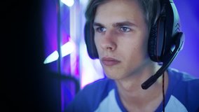 Close-up Shot of Professional Boy Gamer Plays in Video Game on a eSports Tournament/ in Internet Cafe. He Wears Headphones and Gives Commands into Microphone.