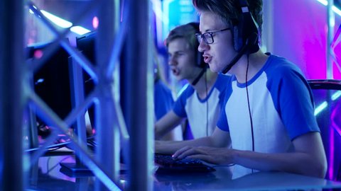 Team of Boys and Girls Gamers Playing in a Multiplayer Video Game Tournament. They use Headsets and Speak Into Microphones. Internet Cafe/ Gaming Arena is Colored in Neon Lights.Shot on RED EPIC-W 8K