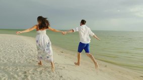 Young couple in love in light clothes carefree running on a clean tropical beach. 4K slow motion video