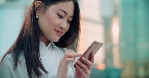 closeup of beautiful young business Asian woman with smartphone texting messenger with skyscrapers in the background
