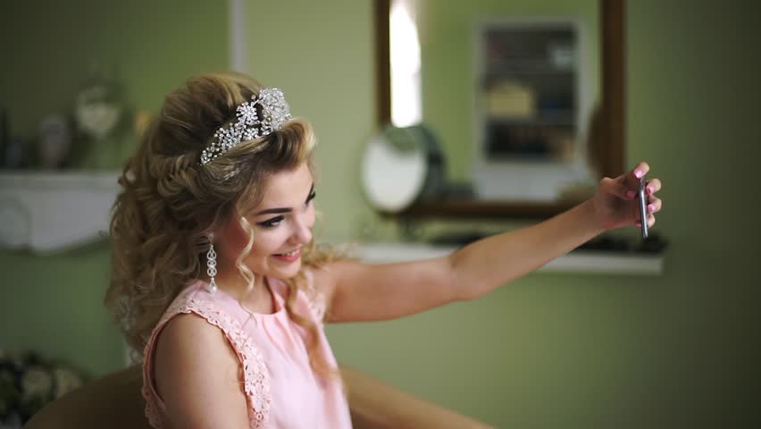 Bride makes selfie his phone. Stylish Woman Fiancee with Bridal Hairstyle, Event Makeup and Jewelry. Big close UP.