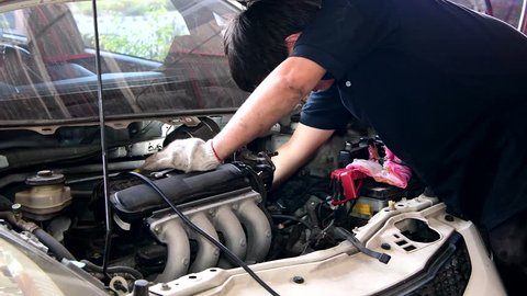 Asian mechanic man checking and maintenance engine in garage.