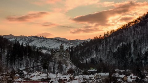 Bran castle at sunset in winter. Panoramic view with dramatic sky at sunset over Bran village, Romania.  4k timelapse. 