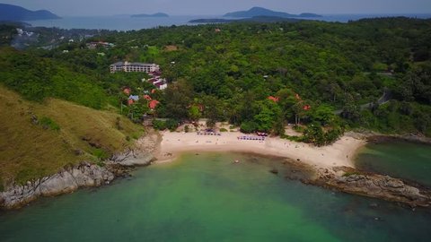 Nice small Ya Nui beach beside tall hill with viewpoint on top, west shore of Phuket Island, aerial shot. Forested area on land, some buildings seen in green. Nice tropical sea waters downwards
