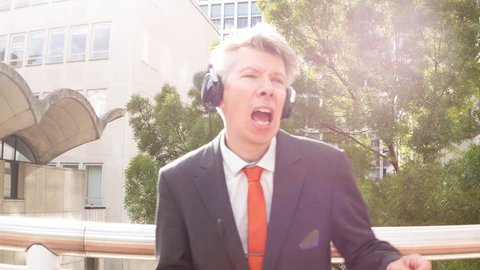 Smart carefree Middle aged caucasian businessman wearing headphones listening to music on MP3 player singing outside the office