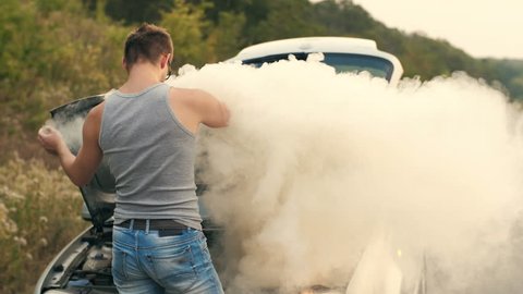 A man looks at a smoking engine of a broken car