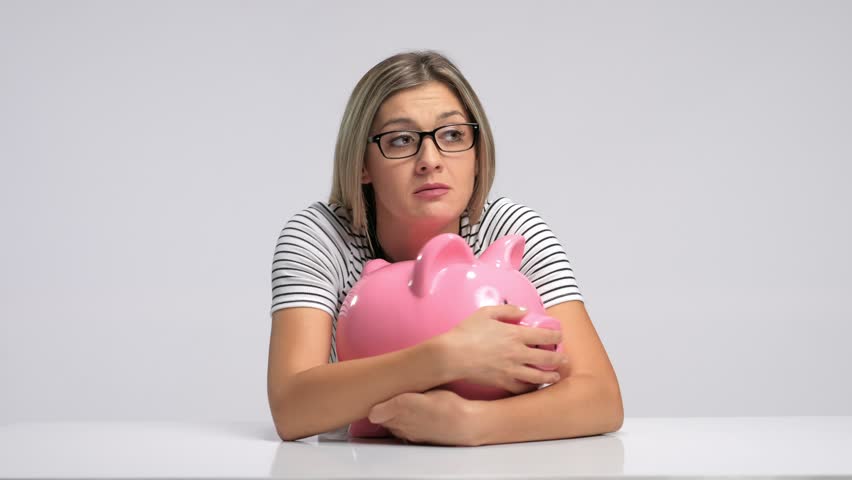 Scared woman trying to protect her piggybank from being stolen against gray background Royalty-Free Stock Footage #30110041