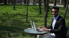 Worker sits on chair by table and using laptop. Man clicking keyboard, closes computer and stands up. Guy has beard, short hair and dimples on cheeks. Man dressed in black jacket, white jeans and blue - Powered by Shutterstock - Get 15% off with code: PIKWIZARD15
