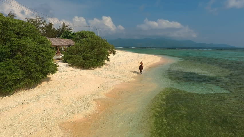 Aerial view of indonesian man riding black horse on beach