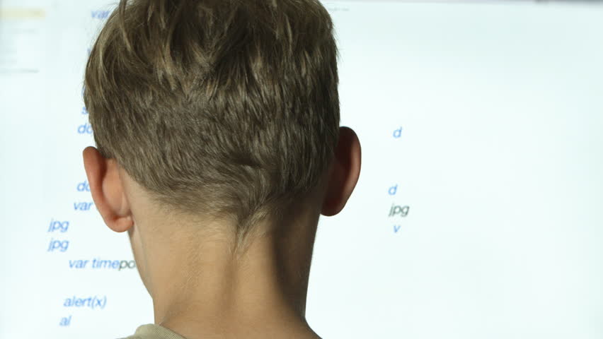 A young male child writing code on a computer screen close up from behind the head.
