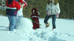 Family having fun together making a snowman near winter forest