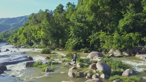 HON BA/VIETNAM - JULY 08 2017: Drone shows local man crossing mountain river streaming under sunshine among rocks against pictorial nature on July 08 in Hon Ba