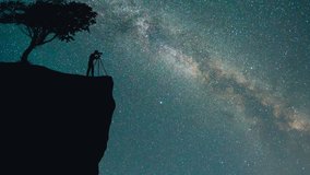 The man with a camera stand on the mountain against a sky with stars. time lapse