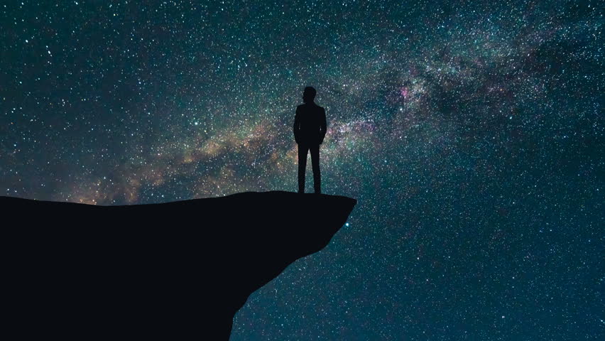 The man stand on the top of a mountain on a starry sky background. time lapse