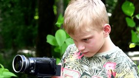 Young boy with video camera shoots film in nature of green park slow motion. Children outdoors in summer are creative work of cinema. Beautiful footage. Interesting to look at world in childhood.
