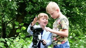 Young two boys with video camera shoots film about nature of green park. Children outdoors in summer are creative work of cinema. Beautiful footage. Interesting to look at world in childhood.