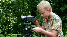 Young boy with video camera shoots film about nature of green park background. Children outdoors in summer are creative work of cinema. Beautiful footage. Interesting to look at world in childhood.