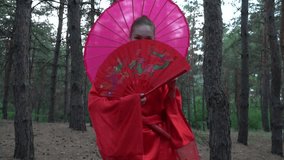 A beautiful geisha in a red kimono looking at the camera and walking in a coniferous forest, slow motion