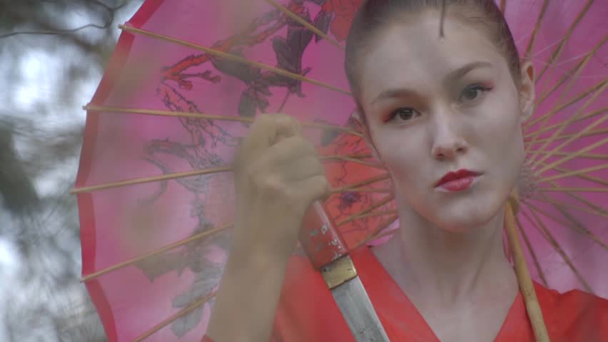 geisha in a red kimono with a tanto dagger in his hand gazing intently into the camera, slow motion