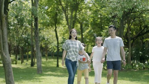 asian family of 4 walking & laughing in park in sunny summer in slow motion