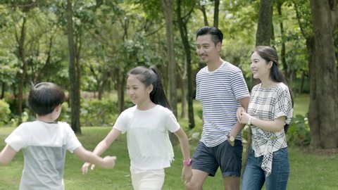 asian family of 4 walking & laughing in park in sunny summer in slow motion