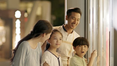 asian family of 4 standing & looking into shop window in slow motion 库存视频
