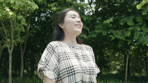 pretty asian woman taking deep breath, smiling & enjoying nature outdoor