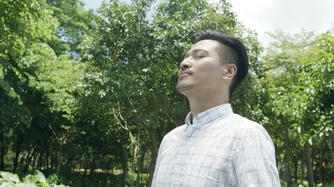 asian man taking deep breath, smiling & enjoying nature outdoor in slow motion