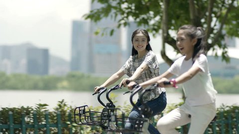 asian mother & daughter cycling on lakeside promenade in summer