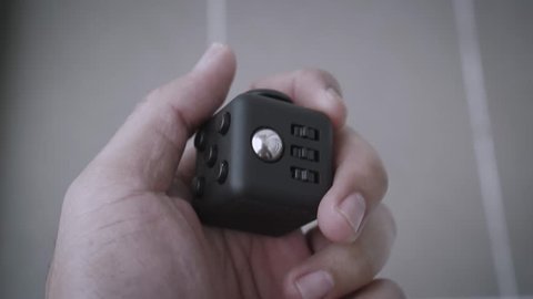 Footage of man holding Fidget Cube stress reliever in hand over grey tiles