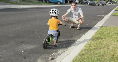 Father teaching toddler son to ride bicycle balance bike- father coaxing son