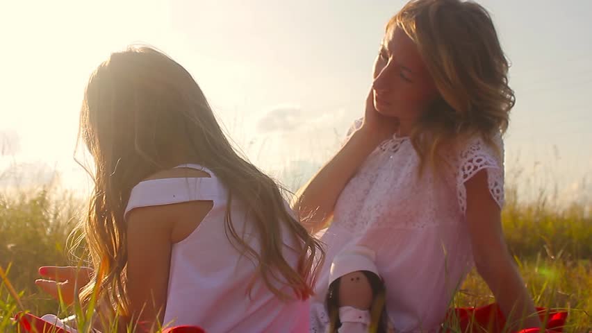 Happy mother with cute little daughter lying down on fresh green grass field, spending time together outdoors, enjoying summer holidays
