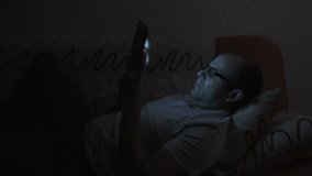 Close up of man with glasses using smartphone. Young man with tablet computer. A man at night on social networks using a smartphone. Man with tablet computer lying on sofa