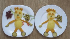 A woman is making a funny man on a plate of vegetables. Cheerful vegetable salad from potatoes carrots peas, cucumber and beets