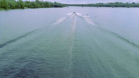 Flying over wakeboarding on river 4k aerial video. Wakeboarder surfing behind boat trails and doing tricks: somersault flip jump