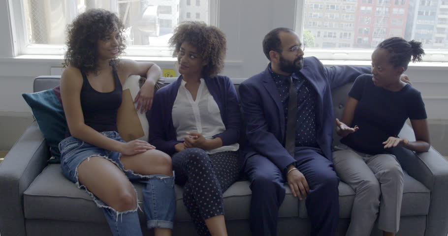 Mixed race group of friends chatting and hanging out on a sofa in a bright, day interior, urban loft or apartment. Parts of Los Angeles city visible through windows. Slow motion hand-held 4K | Shutterstock HD Video #30183403