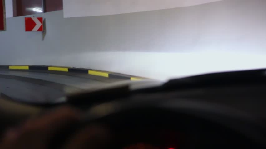 Driver hands rotate steering wheel of car which rides by curvy way out from underground garage