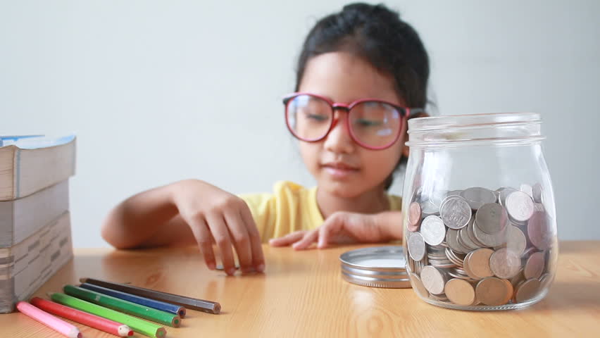 Asian little girl putting the coin into a  clear glass jar on table metaphor saving money concept with sound select focus on jar | Shutterstock HD Video #30196330