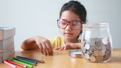 Asian little girl putting the coin into a  clear glass jar on table metaphor saving money concept with sound select focus on jar