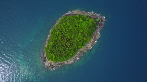 Small island covered with tropical rainforest, stone shore belt around woods, top-down aerial view. Nice crystal water of Andaman sea surround isle. Calm surface, small waves wash rocky beach