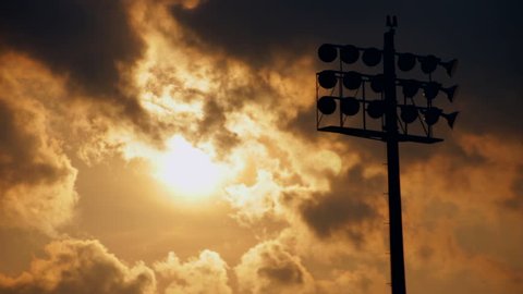 Timelapse of sun setting behind a cloudscape and a silhouetted stadium light.