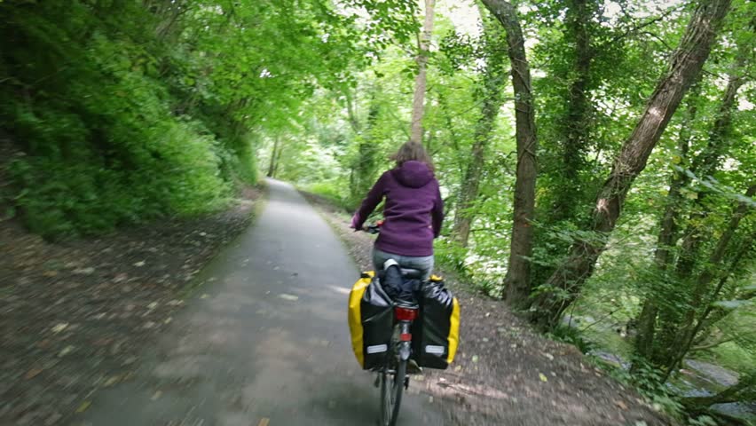 Woman on a bike drive bicycle over cycle path with a lush green forest around. POV behind the cyclist