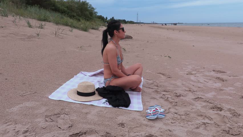 Woman in bikini sits on beach
