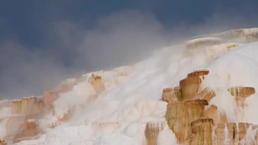 The backside of Mammoth Hot Springs in Yellowstone National Park, Montana with geothermal hot springs water running down the travertine terraces with steam drifting up in the atmosphere.