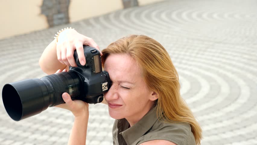 A close-up of a female photographer is taking pictures in the street with the help of a professional camera. 4k, slow motion