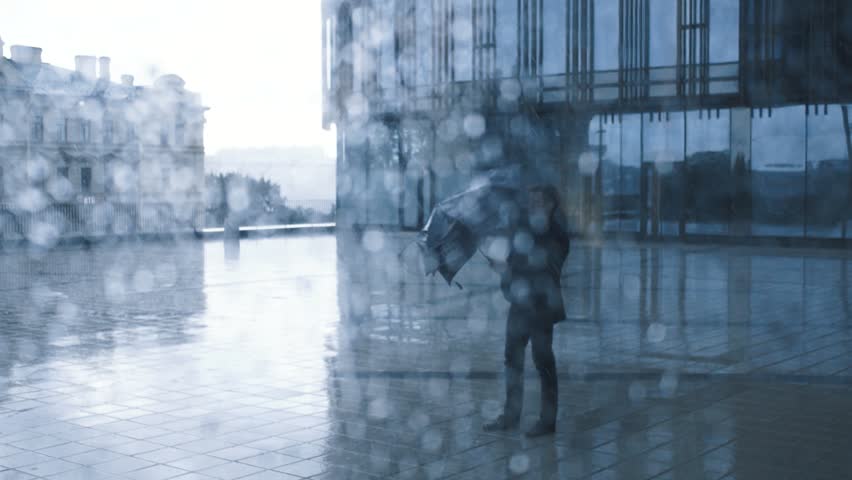 Young businessman in suit with umbrella under rain. Business centre building at the background. View through window with drops of water. The gust of wind pulls the umbrella out of hand Royalty-Free Stock Footage #30220522