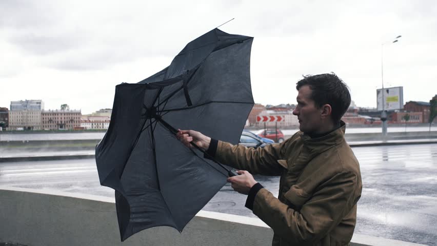 Man in jacket with umbrella standing outdoors. The gust of wind pulls umbrella out of hand | Shutterstock HD Video #30220543