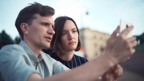 Young millennial couple watching videos on smartphone together in the park. Young couple using smartphone together outdoor in the city.