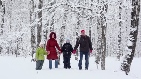 Parents with their kids stand under snow falls at winter day in park, then father and son start beat tree stem for make snowfall